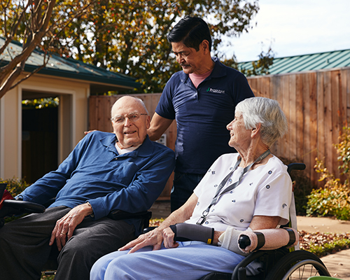caregiver with couple sitting in courtyard