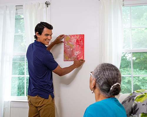 caregiver helping hang painting on wall